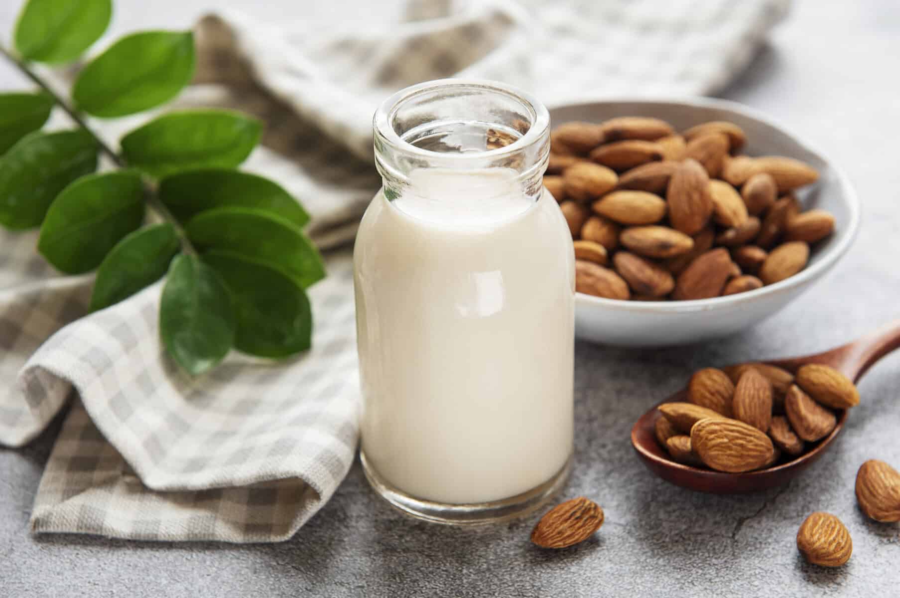 Glass jar of homemade almond milk with almonds and green leaves.