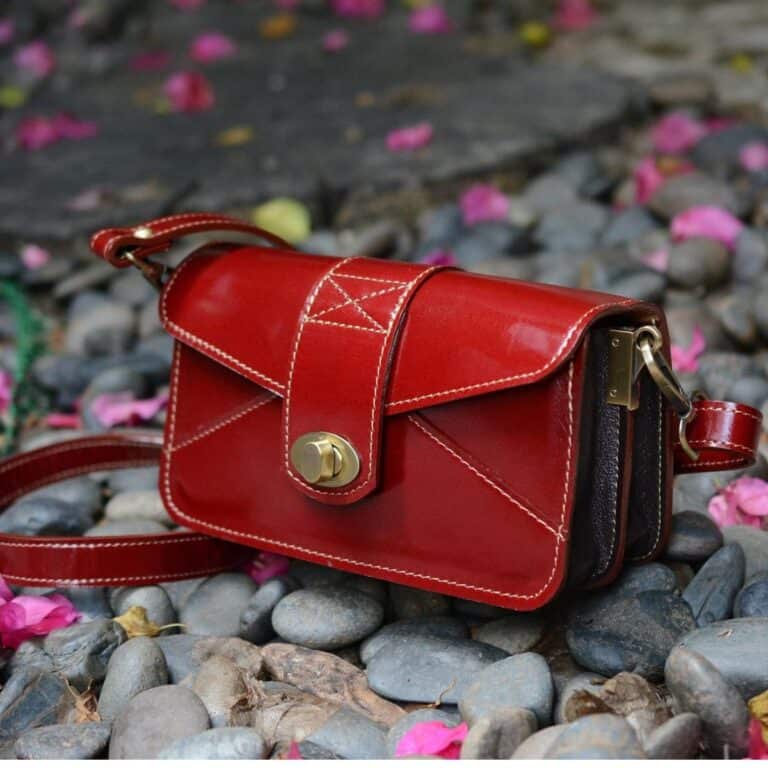 Red vegan leather handbag with gold accents on rocky ground.