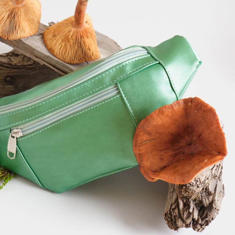 Green vegan leather fanny pack with mushrooms on a wooden surface.