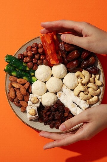 Colorful vegan snack platter with nuts, dates, and fruit on orange background.