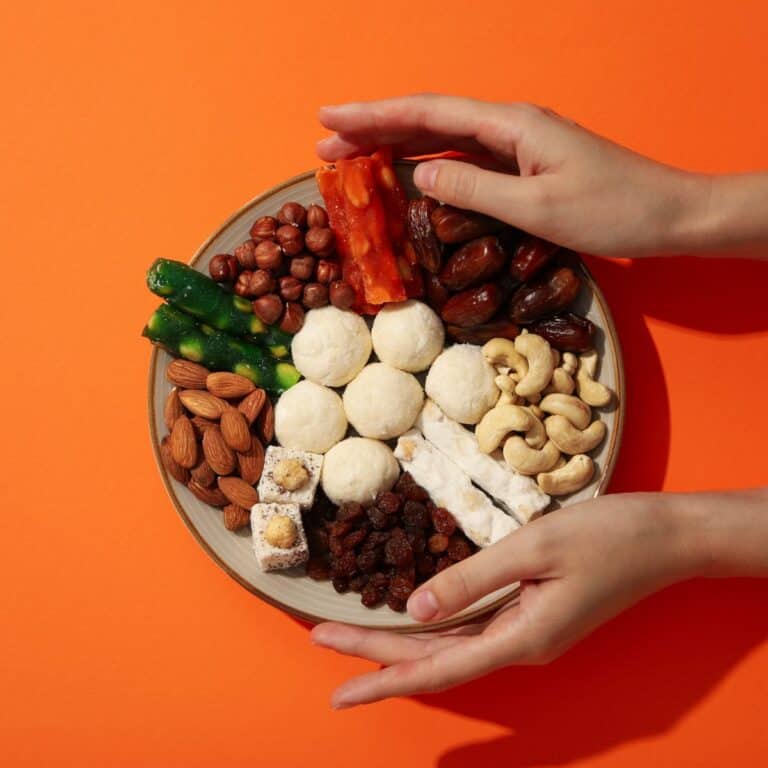 Colorful vegan snack platter with nuts, dates, and fruit on orange background.