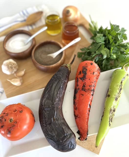 Fresh eggplant, carrots, and tomato for vegan cooking on a white platter.