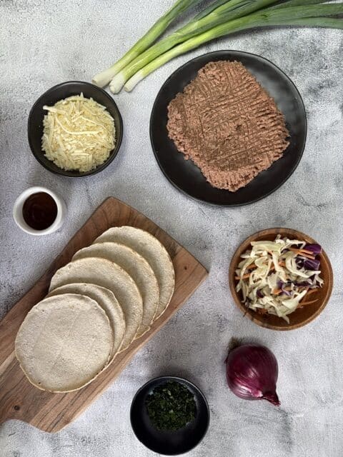 Vegan taco ingredients including shredded vegan cheese, vegan mince,tortillas, and vegetables.