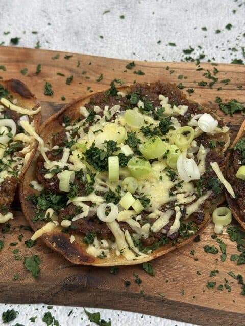 Vegan smashburgers topped with vegan cheese, green onions, and herbs on a wooden board.