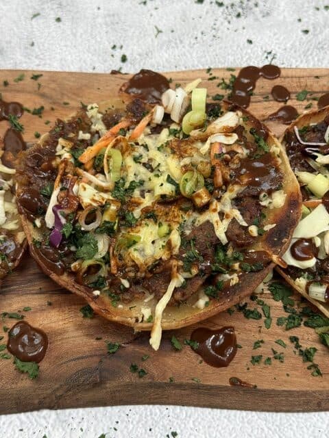 Vegan nachos topped with vegetables, vegan cheese, and bbq sauce on a wooden board.