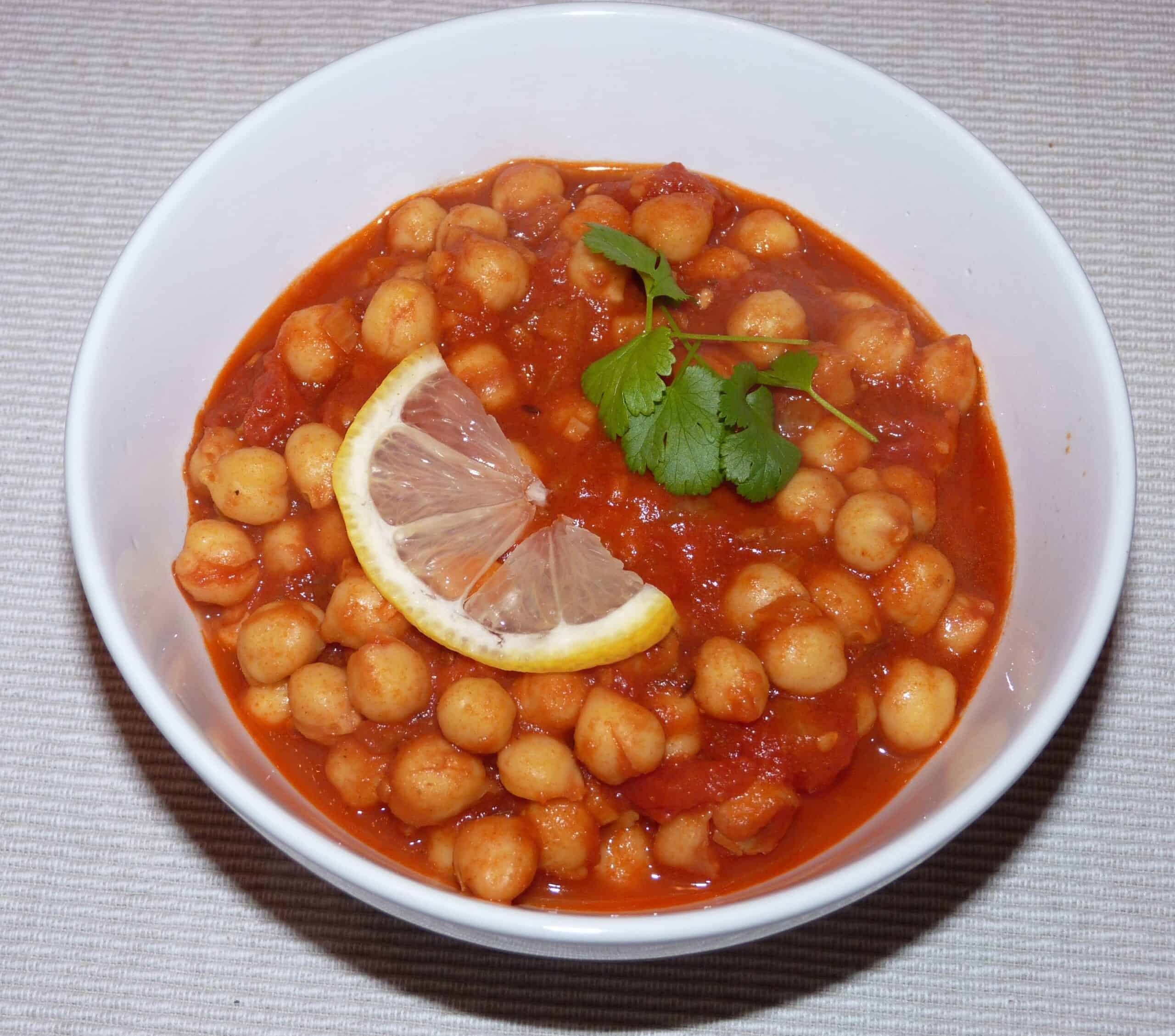 Vegan chickpea curry in a white bowl garnished with lemon and cilantro.