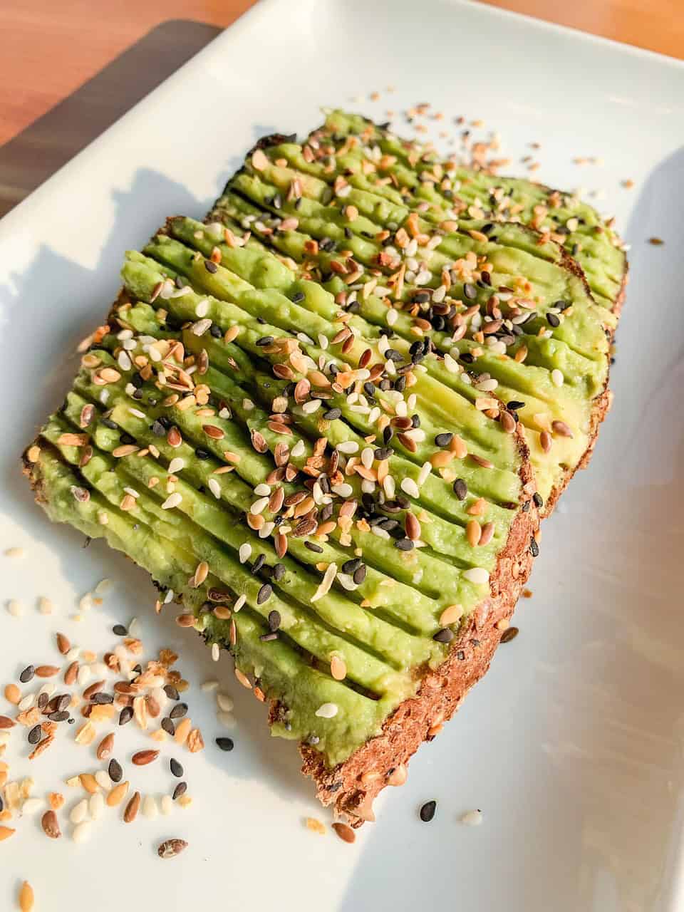 Vegan avocado toast topped with seeds on a white plate.